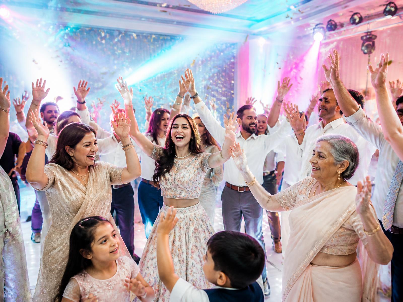 Guests of all ages dancing with hands up under turquoise and magenta lights as confetti falls
